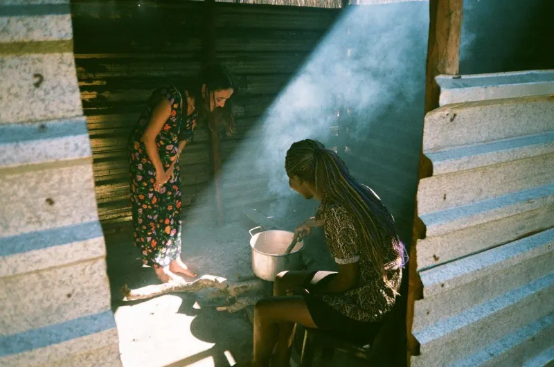 A woman cooking over a fire in a sunlit kitchen