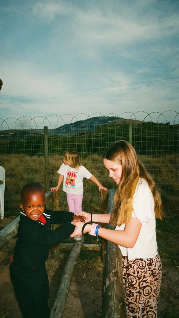 A volunteer playing with two children outside the school